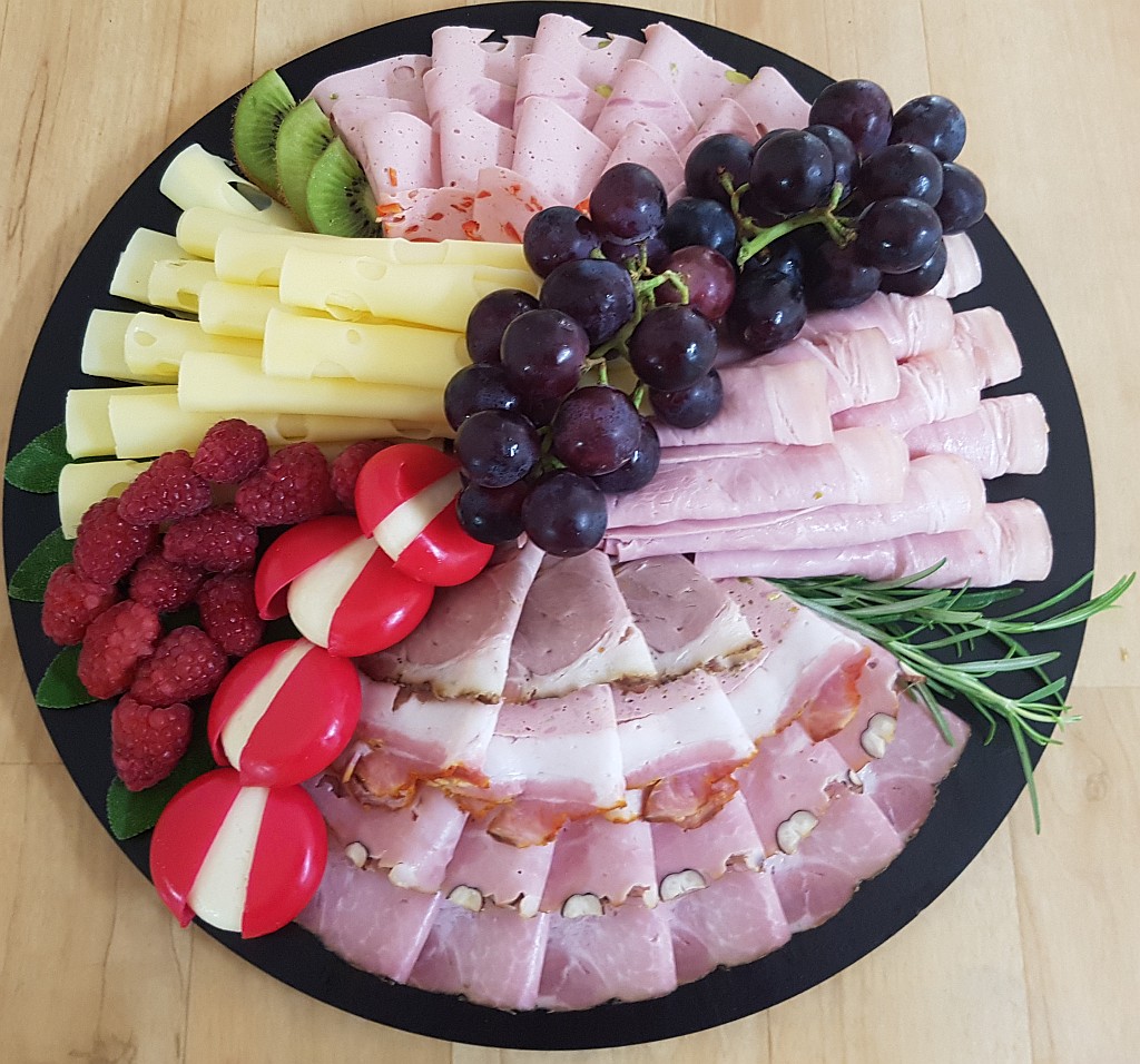 Käse-Wurst-Platte mit verschiedenen Sorten Obst und Kräutern